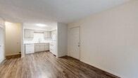 This single-floor 1-bedroom, 1-bathroom unit offers a clean, functional layout designed for comfortable everyday living. The living area is bright and open, featuring dark wood-style laminate flooring that runs throughout the main spaces, neutral light-colored walls, and a textured ceiling. A standout feature of the living room is the sliding glass door that fills the space with natural light and provides direct access to an outdoor area with views of surrounding greenery.

The kitchen is open to the main living space and is equipped with gray cabinetry, white appliances including a refrigerator, electric range with overhead ventilation, and a dishwasher. A stainless steel sink is positioned beneath upper cabinets, offering ample storage and counter space for meal preparation.

A hallway connects the main living area to the bedroom and bathroom. The bedroom features plush carpeting, a window with blinds for natural light and privacy, and a quiet, restful atmosphere. The bathroom includes a full tub and shower combo with a curved curtain rod, clean white surround, and chrome fixtures, complemented by wood-style flooring. The unit also includes a louvered closet door, adding practical storage throughout.