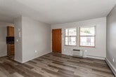 This single-floor residence offers a practical and comfortable layout with thoughtful finishes throughout. The main living area welcomes you through a warm wood-toned entry door and features light hardwood-style flooring that extends through much of the space, neutral-toned walls, and a textured ceiling. A wall-mounted HVAC unit provides climate control, and windows allow natural light to filter in with views of the surrounding neighborhood. The galley-style kitchen is efficiently designed with warm oak cabinetry, dark granite-style countertops, a dark tile backsplash, a stainless steel sink, and a full suite of appliances including a refrigerator, electric range, and built-in microwave. A window above the sink brings in additional natural light. The bathroom is outfitted with a full tub and shower combination featuring classic white tile with decorative accents, a toilet, and a vanity with white cabinetry and a dark countertop paired with a wall-mounted mirror and chrome shelving. The bedroom includes plush neutral carpeting and a ceiling fan with an integrated light fixture, offering a cozy and restful atmosphere. An additional room with hardwood-style flooring and a baseboard heater provides flexible use as a second bedroom or dedicated workspace. Overall, the space presents a clean, move-in-ready environment with functional design throughout.