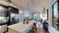 Located in Houston's vibrant Montrose neighborhood, this 2-bedroom, 2-bathroom residence offers a thoughtfully designed open-concept layout that seamlessly connects the kitchen, dining, and living areas. Rich hardwood floors flow throughout the main living spaces, complemented by abundant natural light streaming through multiple large windows with elegant draping curtains.

The kitchen is a standout feature, boasting dark espresso cabinetry, stainless steel appliances, a subway tile backsplash, and a generous quartz-topped island with bar seating — ideal for casual dining or entertaining. Pendant lighting and track lighting add a polished finish. The adjacent dining area offers ample space for a full dining set, with room for a dedicated workspace nearby.

The primary bedroom is a serene retreat with plush carpeting, a ceiling fan, and sliding glass doors opening to a private balcony with lush outdoor views. It includes a spacious walk-in closet with wire shelving. The second bedroom is equally comfortable, featuring soft carpet and ceiling fan. Both bathrooms are well-finished, with the primary bath showcasing granite countertops, a walk-in glass shower, and large-format tile flooring. Two closets provide generous storage throughout the residence.