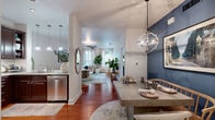 This thoughtfully designed single-floor residence offers a seamless blend of comfort and style across its open-concept layout. Entry is welcomed by light hardwood flooring that transitions into rich, warm-toned hardwood running through the main living areas. The dining area is highlighted by a statement orb chandelier and a bold navy accent wall, creating a sophisticated focal point adjacent to the kitchen. The kitchen is well-equipped with dark espresso cabinetry extending to the ceiling, granite countertops, a classic subway tile backsplash, and a full suite of stainless steel appliances including a gas range and French door refrigerator. The spacious living room enjoys abundant natural light through large windows and features a ceiling fan, creating a bright and airy atmosphere. Both bedrooms are generously sized with plush carpet flooring, ceiling fans, and windows that invite natural light. The primary bedroom offers ample space for a full furniture arrangement. The bathroom is finished with large-format white tile, a granite-topped vanity with rich wood cabinetry, and a combined tub and separate walk-in shower. Throughout the residence, neutral wall tones and clean white trim create a cohesive, inviting ambiance.