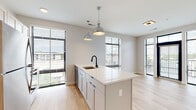 Located at 300 E Fifth Ave in Columbus, Ohio, this single-floor residence offers a clean, contemporary design with a cohesive aesthetic carried throughout every room. The open-concept kitchen serves as the heart of the home, centered around a generous island with a white quartz countertop, an undermount sink with a matte black faucet, and white shaker-style cabinetry accented with blue hardware. A full suite of stainless steel appliances — including a refrigerator, range, and microwave — complete the space, while a pair of industrial-style pendant lights add character overhead. Large windows with horizontal blinds flood the area with natural light and provide views of the surrounding Columbus neighborhood. Light hardwood flooring runs continuously throughout, tying the spaces together seamlessly. A well-proportioned hallway connects the main living area to the private rooms, lined with louvered and panel doors offering access to closets and additional rooms. Bedrooms feature sliding panel doors revealing built-in closet shelving. The bathrooms showcase a consistent design language, with vertically stacked white subway tile, matte black fixtures, and hardwood-style flooring — one bathroom features a walk-in glass-enclosed shower, while another offers a full tub and shower combination.