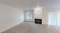 Located in Fife, WA, this 2-bedroom, 2-bathroom residence offers a well-organized single-level layout designed for comfortable everyday living. The living room serves as the heart of the home, anchored by a built-in fireplace with an arched alcove above, soft carpeting underfoot, and a window that draws in natural light. Adjacent to the living area, the kitchen features warm wood cabinetry, stainless steel appliances including a dishwasher, refrigerator, and microwave, along with light hardwood-style flooring and track lighting overhead. A charming arched pass-through window connects the kitchen to the main living space, enhancing the open feel. The primary bedroom is a comfortable retreat with carpeted flooring, a window with outdoor views, and a baseboard heating unit. It is served by a dedicated bathroom equipped with a glass-enclosed walk-in shower. The second bedroom also features plush carpeting and a closet with sliding doors. A second full bathroom includes a tiled tub-shower combination with a curved curtain rod and chrome fixtures. Additional storage is provided by an in-unit closet. The unit's clean white walls and neutral palette create a bright, move-in-ready atmosphere throughout.