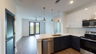 This single-floor apartment at 44 Braves Ave in Lawrenceville, GA offers a thoughtfully designed modern living space. The open-concept kitchen and living area serve as the heart of the unit, featuring two-tone cabinetry with dark lower and white upper cabinets, white quartz countertops, a subway tile backsplash, and a peninsula island with an undermount sink. Three polished pendant lights hang above the island, adding a stylish focal point. Stainless steel appliances include a side-by-side refrigerator with ice maker, electric range, over-the-range microwave, and dishwasher. Wood-look flooring runs throughout the kitchen and living area, which opens to a private balcony through glass-paneled French doors, allowing abundant natural light. The bedrooms are carpeted and bright, each featuring windows with views of surrounding greenery and ceiling fans for comfort. The primary bathroom offers a long vanity with white countertop, dark cabinetry, wood-look flooring, and access to a walk-in closet. A second bathroom provides a full soaking tub and shower combo with clean white tile. The unit presents a clean, contemporary aesthetic throughout.