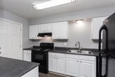 Located at 881 E Holly St in Boise, Idaho, this single-floor unit offers a clean, functional layout with a neutral gray color palette throughout. The living area features durable wood-look plank flooring, gray walls, and a textured ceiling, creating a bright and open atmosphere. Multiple windows dressed with horizontal blinds allow natural light to filter in, with views of surrounding greenery.

The kitchen is well-appointed with white shaker-style cabinetry, dark granite-look countertops, and black appliances including a range with overhead ventilation and a refrigerator. A pass-through counter connects the kitchen to the adjacent living and dining area, enhancing the open flow of the space.

The bedrooms are carpeted for comfort and each features louvered bifold closet doors providing ample built-in storage. The soft neutral carpet complements the gray walls and textured ceilings consistent throughout the unit.

The bathroom includes a white vanity with an overhead mirror, a tub-shower combination clad in large-format dark gray tile, and clean, modern finishes that give the space a contemporary feel.

Overall, this unit presents a cohesive, move-in-ready interior with practical finishes and a straightforward, efficient floor plan suited for everyday living in a convenient Boise location.