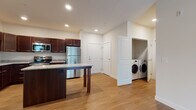 Located at 2001 Traceway Dr in Fitchburg, Wisconsin, this single-floor unit offers a thoughtfully designed layout with cohesive finishes throughout. The kitchen serves as a central highlight, showcasing rich dark-stained cabinetry, granite countertops, and a full suite of stainless steel appliances including a refrigerator, range, microwave, and dishwasher. A substantial kitchen island with a matching granite surface provides additional prep space and casual seating. Warm hardwood-style flooring runs seamlessly throughout the main living areas, lending a clean and unified aesthetic. A dedicated in-unit laundry closet is conveniently positioned near the kitchen and entry, housing a full-sized washer and dryer side by side. The unit includes two bathrooms, each finished with granite-topped dark wood vanities and hardwood-style flooring. Both bathrooms are equipped with accessibility features, including multiple stainless steel grab bars near the toilet and tub/shower combination, making the space functional for a wide range of residents. The neutral, light-toned walls complement the darker cabinetry and warm flooring, creating a balanced and inviting atmosphere. Recessed lighting throughout ensures bright, even illumination across all areas of the unit.