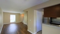 This two-story residence offers a well-organized and functional layout designed to maximize livability across both levels. The main floor greets visitors with a spacious, open-concept living area bathed in natural light from a large window, creating a bright and welcoming atmosphere. Rich, dark hardwood-style flooring runs throughout the main living space, adding warmth and a sense of continuity to the area.

A staircase with a classic white banister connects the two floors and is neatly positioned near the entryway, allowing for an efficient flow between levels. The front entry door is clearly visible from the main living area, contributing to an open sightline throughout the space.

Adjacent to the living area, the kitchen features warm wood cabinetry, light granite countertops, and stainless steel appliances, including a full-size refrigerator. The kitchen transitions smoothly from tile flooring, distinguishing it from the main living area while maintaining a cohesive design aesthetic. A louvered closet door nearby provides convenient built-in storage on the main level.

The neutral, beige-toned walls throughout the space offer a versatile backdrop suited to a variety of interior styles. The overall ambiance is clean, understated, and move-in ready, making this a practical and comfortable two-floor home.