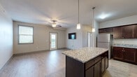 This well-appointed 2-bedroom, 2-bathroom unit at 5456-301 Mortensen Road in Ames, Iowa offers a thoughtfully designed single-floor layout with a generous overall footprint. The kitchen is a standout feature, showcasing rich dark wood cabinetry, granite countertops, a large center island, and a full suite of stainless steel appliances including a refrigerator, electric range, microwave, and dishwasher. Light wood-style luxury flooring runs throughout the kitchen and living areas, lending warmth and a cohesive aesthetic to the open-concept space. The living room features a ceiling fan and a glass exterior door that brings in natural light and provides outdoor access. The spacious primary bedroom is carpeted for comfort and includes a dedicated closet as well as access to a private en-suite bathroom with a walk-in shower and granite-topped vanity. The second bedroom also features carpet, a ceiling fan, a window with natural light, and wood-style flooring as an option. The second full bathroom includes a tub-shower combo and a matching dark wood vanity with granite countertop. A dedicated laundry room houses a stacked washer and dryer unit, adding everyday convenience. Two closets throughout the unit offer ample storage.