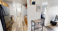 This efficient single-floor residence offers three bedrooms and two full bathrooms within a well-organized floor plan. The layout is anchored by a central hallway with light wood-style flooring that connects the key living spaces, lending a cohesive flow throughout. The kitchen features warm wood cabinetry and stone-look countertops, positioned along the hallway corridor for easy access. Adjacent to the kitchen, the living room is a bright, clean space with light wood flooring, a window overlooking the outdoors, and a baseboard heating system. The bedrooms are carpeted and finished in soft neutral tones. The primary bedroom offers a closet, a window with outdoor views, and a wall-mounted air conditioning unit. The additional bedrooms share similar finishes, each with windows that allow natural light. The two bathrooms are clean and functional, each featuring a vanity with wood cabinetry, a toilet, and a shower/tub combo. Throughout the unit, the white walls and recessed lighting create a bright, consistent atmosphere. Modern abstract wall art accents the common areas, adding a contemporary touch to the otherwise straightforward design. Overall, the space prioritizes practicality and comfort in a compact, well-connected layout.