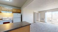 Located at 1039 S Parker Rd in Denver, Colorado, this single-floor unit offers a practical and functional layout with a seamless flow between the kitchen, living, and sleeping areas. The kitchen is equipped with warm honey-toned wood cabinetry, a white electric range, a full-size refrigerator, and a peninsula island with a dark laminate countertop that serves as both a prep area and a casual dining surface. The kitchen features hardwood-style flooring that transitions into plush carpeting throughout the living room and bedroom. The living area is bright and open, featuring a wall-mounted air conditioning unit, baseboard heating, a textured ceiling, and a sliding glass door that opens onto a private balcony, allowing natural light to fill the space and providing views of the surrounding area. The bedroom is a generously sized, quiet retreat with soft carpeting, neutral-toned walls, and additional baseboard heating. The bathroom includes a full tub and shower combination with white tile surround, brushed nickel fixtures, a toilet, and a vanity with a stone-finish countertop and hardwood-style flooring. Throughout the unit, the neutral color palette and clean finishes create a cohesive and functional living environment well-suited for everyday comfort in a convenient Denver location.