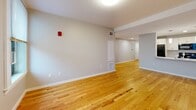 Located at 10 Main St in Fitchburg, MA, this single-floor, 2-bedroom, 1-bathroom unit offers a well-organized layout finished with warm hardwood flooring throughout. The open-concept living and kitchen area provides a functional, connected space ideal for everyday living. The kitchen is equipped with white cabinetry, light stone-toned countertops, a stainless steel sink set in an island-style peninsula, and black appliances including a refrigerator, electric range, and over-the-range microwave. Neutral gray walls complement the warm wood tones across the unit.

The primary bedroom is a generously sized room featuring two windows that bring in natural light and views of the surrounding neighborhood. The second bedroom also benefits from natural light via its own window. Both bedrooms are serviced by dedicated closets outfitted with wire shelving systems for organized storage.

The full bathroom includes a single-vanity with cabinetry, a wall mirror, recessed lighting, and a tub and shower combination with a sliding glass door. Neutral tile flooring completes the clean, functional aesthetic. The overall design of the unit is clean and modern, with consistent finishes throughout.