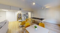 Located at 1228 Spruce Street in Philadelphia's vibrant Washington Square West neighborhood, this single-floor space offers a well-organized layout comprising a living room, game room, bedroom, and hallway. Light hardwood flooring flows consistently throughout, lending a clean and cohesive aesthetic to every room.

The living room is a welcoming, well-lit area characterized by a striking blue accent wall that adds depth and personality. Track lighting and large windows allow natural light to fill the space, while the open layout comfortably accommodates a full seating arrangement, media console, and coffee table.

Adjacent to the living room, the game room is a standout feature of this space. It is generously proportioned, with a full-size pool table as its centerpiece. Wide horizontal windows line one wall, bringing in ample natural light and views of the surrounding streetscape. Track lighting overhead and arched built-in shelving add both function and character, while café-style seating tables and chairs make it an ideal social and recreational area.

The bedroom offers a private, compact retreat, while the hallway provides a clean transition between the rooms. Throughout the space, the combination of white walls, blue accents, and warm wood floors creates a modern yet approachable atmosphere suited for both relaxation and entertainment.
