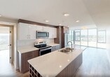 Located at 2610 109 Street NW in Edmonton, Alberta, this well-designed two-bedroom, two-bathroom unit offers a thoughtful layout across a single floor. Light wood-tone flooring runs throughout, complementing the clean, neutral palette of white and soft grey tones that define the interior.

The open-concept kitchen is a standout feature, boasting a two-toned design with warm wood lower cabinetry paired with white upper cabinets. A generous island with a light quartz countertop and double stainless steel sink anchors the space, while stainless steel appliances — including a range, microwave, and refrigerator — complete the functional setup. Recessed lighting overhead adds a polished finish.

Floor-to-ceiling windows in the living area and bedrooms flood the space with natural light and frame elevated views of the surrounding Edmonton cityscape and open landscape. The primary bedroom is comfortably sized and benefits from these expansive windows, with a sliding glass door providing access to the outdoors.

Both bathrooms are finished in a clean, contemporary style, featuring white vanities with light countertops and wood-tone flooring. One bathroom includes a wall-mounted grab bar. Three closets offer generous storage throughout, and an in-unit laundry area adds everyday convenience. The hallway connects all spaces efficiently, maintaining a cohesive and airy feel throughout.