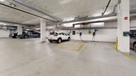 Located at 2540–2590 Lonsdale Ave in North Vancouver, BC, this underground parking garage offers a generously sized, single-level facility designed to accommodate modern parking needs. The space features a polished concrete floor with clearly defined yellow stall markings and designated accessible parking areas, ensuring organized and efficient use throughout.

Overhead, exposed mechanical systems including ventilation ducts, fire suppression piping, and fluorescent lighting run across the ceiling, providing both functionality and clear visibility throughout the garage. Structural concrete columns are positioned throughout and painted white to enhance brightness in the interior environment.

A standout feature of this facility is the presence of multiple electric vehicle (EV) charging stations, labeled and positioned at several stalls, reflecting a commitment to sustainable transportation infrastructure. Safety is addressed through strategically placed convex mirrors, emergency exit signage, and a fire alarm pull station.

Access to the garage is provided via a full-width roll-up garage door that opens to an exterior ramp, offering a smooth transition between the parking level and the street. Interior access doors connect to the building's main areas, and a secured gated section provides additional separated storage or parking capacity. The facility is well-maintained, clean, and clearly designed to serve a modern residential or mixed-use building.