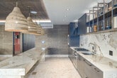 Located at 3775 Sixth Avenue in San Diego's vibrant Hillcrest neighborhood, this thoughtfully designed single-floor space offers a generous and versatile layout that seamlessly blends indoor and outdoor living. The interior is anchored by a striking open-plan layout with rich wood-paneled ceilings accented by warm cove lighting, polished terrazzo flooring, and floor-to-ceiling glass walls that flood the space with natural light and frame views of the adjacent outdoor patio.

The gourmet kitchen is a standout feature, outfitted with sleek wood cabinetry, a dramatic marble slab backsplash, stone countertops, a stainless steel gas cooktop, built-in oven, and an undermount sink. A long communal island with bar seating sits beneath a trio of woven pendant lights, making it ideal for both cooking and gathering. Open shelving along the back wall provides both storage and display space.

The lounge and dining areas are furnished with warm, natural materials — leather sofas, woven rattan chairs, cork ottomans, and a solid wood dining table — creating an inviting, organic aesthetic. Large glass doors open directly to a spacious outdoor terrace featuring a wood-fired pizza oven, an outdoor kitchen with a grill, bar seating, lounge furniture, and a lush living green wall, completing this exceptional communal amenity space.