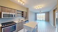 Located at 3300 N Port Royale Drive in Fort Lauderdale, this 1-bedroom, 1-bathroom unit offers a thoughtfully designed layout with modern finishes on a single floor. The open-concept kitchen and living area serves as the heart of the unit, featuring wood-grain cabinetry, open shelving, a light-colored tile backsplash, and stainless steel appliances including a gas range, microwave, dishwasher, and refrigerator. A central kitchen island with a white countertop provides additional workspace and casual dining potential. Track lighting with brass-toned fixtures illuminates both the kitchen and living area, which extends toward a sliding glass door leading to a private balcony, allowing natural light to flow freely throughout the space. A ceiling fan in the living area adds comfort and airflow. Light-toned tile flooring runs consistently throughout the unit, contributing to a clean, cohesive aesthetic. The bedroom features a large window with horizontal blinds framing outdoor greenery, and is complemented by a generously sized walk-in closet with wire shelving. The bathroom is well-appointed with a wood-toned vanity, white quartz countertop, large mirror, modern light fixtures, and a tiled tub-shower combination.