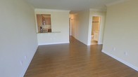 This single-floor residence offers a clean, open layout designed for comfortable everyday living. The spacious main living area is finished with warm wood-style flooring that extends throughout, complemented by crisp crown molding that adds a refined architectural touch to the neutral, light-toned walls.

The kitchen is positioned adjacent to the living area and features a raised breakfast bar with granite countertops, a tile backsplash, and warm wood cabinetry, creating an efficient and stylish cooking space. The bar-height counter serves as a natural divider between the kitchen and living area while maintaining an open, connected feel.

A hallway leads from the main living space to additional rooms and a bathroom. The bathroom, visible from the hallway, is well-lit and outfitted with white cabinetry, providing a clean and functional design. Closet space is also accessible along the hallway, offering practical built-in storage.

The overall ambiance of the space is bright, airy, and move-in ready, with consistent finishes and a neutral palette that lends itself well to a variety of interior styles. The open floor plan and cohesive design elements make this a versatile and welcoming residence.