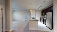 This single-story residence is designed with a functional, open-concept layout that connects the kitchen and living areas seamlessly. The kitchen is a standout feature, equipped with dark espresso cabinetry, stainless steel appliances including a refrigerator, range, and microwave, and granite countertops that extend across a peninsula with an integrated sink. Pendant lighting and a track lighting system illuminate the workspace, while tile flooring grounds the area.

The adjacent living space is generously sized, finished with neutral-toned carpet and a ceiling fan, and features a door providing outdoor access with natural light from the accompanying window. Multiple bedrooms continue the carpeted aesthetic, each fitted with ceiling fans and windows that bring in natural light. One bedroom offers direct access to a dedicated laundry room with a full-size washer and dryer.

The residence includes two bathrooms: one with a tiled walk-in shower and granite vanity, and another with a tub/shower combination and matching finishes. A spacious walk-in closet with wire shelving provides ample storage. Throughout, neutral walls and consistent finishes create a cohesive, understated ambiance.