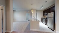 This single-story residence is designed with a functional, open-concept layout that connects the kitchen and living areas seamlessly. The kitchen is a standout feature, equipped with dark espresso cabinetry, stainless steel appliances including a refrigerator, range, and microwave, and granite countertops that extend across a peninsula with an integrated sink. Pendant lighting and a track lighting system illuminate the workspace, while tile flooring grounds the area.

The adjacent living space is generously sized, finished with neutral-toned carpet and a ceiling fan, and features a door providing outdoor access with natural light from the accompanying window. Multiple bedrooms continue the carpeted aesthetic, each fitted with ceiling fans and windows that bring in natural light. One bedroom offers direct access to a dedicated laundry room with a full-size washer and dryer.

The residence includes two bathrooms: one with a tiled walk-in shower and granite vanity, and another with a tub/shower combination and matching finishes. A spacious walk-in closet with wire shelving provides ample storage. Throughout, neutral walls and consistent finishes create a cohesive, understated ambiance.