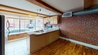 Located at 317 Oliver Hill Way in the heart of Richmond, VA, this single-floor unit masterfully blends industrial character with functional living. The open layout is anchored by rich hardwood floors and striking exposed wooden ceiling beams that run throughout, lending a warm, loft-inspired aesthetic to the space.

The kitchen is a standout feature, showcasing full-height exposed brick walls that serve as a dramatic backdrop to light maple cabinetry, granite-style countertops, and stainless steel appliances including an electric range and dishwasher. Pendant lighting hangs from the beamed ceiling, while large street-facing windows flood the area with natural light and offer views of the surrounding urban streetscape.

A peninsula counter with built-in cabinetry extends into the living area, where a sleek gas fireplace insert adds warmth and visual interest. Exposed ductwork and industrial-style HVAC elements complement the loft character of the space, maintaining an open, airy feel throughout the main living area.

The bathroom is clean and functional, appointed with light tile flooring, a combination tub and shower with glass sliding doors, a maple vanity with granite-style countertop, and ample mirror space. The overall ambiance of this space is a cohesive blend of historic architectural charm and contemporary convenience, well-suited for those who appreciate urban living with distinctive character.