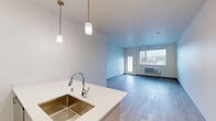 Located at 12608 E Nora Ave in Spokane Valley, WA, this well-designed 2-bedroom, 2-bathroom unit offers a clean, contemporary aesthetic across a single-floor layout. The open-concept kitchen and living area serves as the heart of the home, featuring a large center island with a double stainless steel sink, sleek white quartz countertops, and modern pendant lighting. The kitchen is equipped with stainless steel appliances, including a refrigerator, electric range, and microwave, complemented by contemporary two-tone cabinetry. Light wood-look flooring extends throughout the main living areas, enhancing the bright, airy atmosphere. The living room receives natural light through large windows and a glass-panel door that opens to a private balcony with outdoor views. Both bedrooms are carpeted and offer generous natural light through sizable windows framing views of the surrounding Spokane Valley landscape. The primary bedroom includes its own dedicated bathroom with a light wood vanity and white countertop. A second full bathroom features a tub-shower combination with brushed nickel fixtures and light wood-look flooring. Three closets provide ample storage throughout the unit. The overall design is modern and neutral, creating a clean, move-in-ready environment.