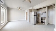 This single-floor unit offers a thoughtfully arranged layout across three distinct areas, making efficient use of its compact footprint. The main living area is bright and open, featuring light gray walls, smooth flooring, and large sliding glass doors alongside multiple windows that fill the space with natural light and provide outdoor views. Two ceiling fans with integrated lighting ensure comfortable airflow throughout, while a wall-mounted mini-split air conditioning unit provides climate control. The kitchen is tucked neatly along one wall and is equipped with stainless steel appliances, including a full-size refrigerator and a stainless range with an electric cooktop. Gray shaker-style cabinetry with brushed nickel hardware, light countertops, and an undermount sink complete the functional kitchen setup. A tall built-in cabinet column near the kitchen provides additional storage. The bathroom features wood-look tile flooring, a pedestal sink with brushed gold fixtures, a full soaking tub with white subway tile surround, and overhead cabinetry for storage. The overall aesthetic is clean and minimal, with a consistent neutral color scheme throughout that creates a cohesive and airy atmosphere.