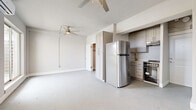 This single-floor unit offers a thoughtfully arranged layout across three distinct areas, making efficient use of its compact footprint. The main living area is bright and open, featuring light gray walls, smooth flooring, and large sliding glass doors alongside multiple windows that fill the space with natural light and provide outdoor views. Two ceiling fans with integrated lighting ensure comfortable airflow throughout, while a wall-mounted mini-split air conditioning unit provides climate control. The kitchen is tucked neatly along one wall and is equipped with stainless steel appliances, including a full-size refrigerator and a stainless range with an electric cooktop. Gray shaker-style cabinetry with brushed nickel hardware, light countertops, and an undermount sink complete the functional kitchen setup. A tall built-in cabinet column near the kitchen provides additional storage. The bathroom features wood-look tile flooring, a pedestal sink with brushed gold fixtures, a full soaking tub with white subway tile surround, and overhead cabinetry for storage. The overall aesthetic is clean and minimal, with a consistent neutral color scheme throughout that creates a cohesive and airy atmosphere.