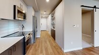 Located in Bellevue, WA, this thoughtfully designed one-bedroom, one-bathroom unit makes excellent use of its compact footprint across a single floor. The open kitchen and living area serves as the heart of the home, featuring warm luxury vinyl plank flooring, recessed lighting, and large windows that invite abundant natural light and views of the surrounding greenery. The kitchen is outfitted with stainless steel appliances including a refrigerator, range, and microwave, complemented by two-tone cabinetry in white and dark gray, quartz countertops, a glass tile backsplash, and a matte black faucet — all lending a clean, contemporary aesthetic. Built-in open shelving adds both storage and character along the main corridor. The bedroom offers plush carpeting, neutral tones, and a dedicated closet, creating a calm and comfortable retreat. The full bathroom is finished with a dark-cabinetry vanity, a backlit mirror, matte black fixtures, and a walk-in shower with a tiled surround set on gray tile flooring. An in-unit laundry area adds everyday convenience. The overall design balances modern style with functional efficiency, making this Bellevue unit a well-appointed and practical living space.