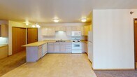 This single-floor unit at 3501 Tenth Ave S in Moorhead, Minnesota offers a practical and well-organized layout across several distinct living areas. The kitchen serves as a central highlight, featuring light oak cabinetry extending to the ceiling for generous storage, warm-toned laminate countertops, a peninsula island ideal for additional workspace or casual dining, and a full suite of white appliances including an electric range with overhead microwave, dishwasher, and refrigerator. A decorative chandelier and flush-mount ceiling lights illuminate the space effectively. The living area is generously proportioned, finished with plush carpet and baseboard heating along the perimeter walls. A sliding glass door admits natural light and provides access to an outdoor space. Additional rooms include carpeted bedrooms, each equipped with ceiling fans, individual windows with blinds, and baseboard heaters for year-round comfort. The unit includes two bathrooms finished with light tile flooring, warm wood-toned vanity cabinetry, and towel bars. Throughout, textured ceilings, warm wood baseboards, and neutral wall tones contribute to a consistent, understated aesthetic.