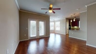 This single-floor, 2-bedroom, 2-bathroom residence offers a thoughtfully designed layout that balances comfort and functionality. The open-concept living and dining area is anchored by rich, dark hardwood flooring that flows throughout the main spaces, complemented by crown molding and ceiling fans that add a polished touch. French doors lead to the exterior, inviting natural light and outdoor views into the living area, while multiple windows with blinds keep the space bright and airy.

The kitchen features bold cherry-toned cabinetry with ample storage, granite-style countertops, black appliances including a range and built-in microwave, and a breakfast bar that connects seamlessly to the living and dining areas. Pendant lighting above the bar adds a warm, modern accent.

Both bedrooms are carpeted for comfort and include ceiling fans and walk-in closets with built-in shelving systems, offering generous storage. The two bathrooms are finished with tile flooring, dark wood vanities, and tub-shower combinations with tile surrounds. A dedicated entryway with a louvered closet door provides a welcoming transition into the main living space. Overall, the residence presents a clean, neutral palette with cohesive finishes throughout.