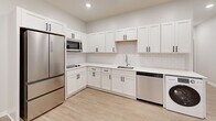 This thoughtfully designed single-floor unit offers a clean, modern aesthetic with a neutral palette and consistent light wood-tone luxury vinyl plank flooring that flows seamlessly throughout the space. The open layout maximizes functionality without sacrificing style.

The kitchen is a standout feature, showcasing white shaker-style cabinetry with matte black hardware, white quartz countertops, and a classic white subway tile backsplash. Stainless steel appliances — including a French door refrigerator, microwave, dishwasher, and an in-unit washer — are thoughtfully integrated. A single-basin sink and ample upper and lower cabinet storage complete this well-appointed space.

The living area is bright and open, illuminated by recessed lighting and a flush-mount ceiling fixture. A window with a roller shade allows for natural light while maintaining privacy. Clean white walls and crisp white baseboards lend a fresh, modern feel to the room.

The bathroom is finished with white shaker-style cabinetry, a undermount sink with white countertop, and a full soaking tub with an overhead shower. Adjacent to the bathroom, a dedicated closet with a hanging rod provides convenient storage. Interior doors throughout feature a paneled design with matte black lever hardware, maintaining a cohesive and contemporary look across the entire unit.