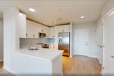 This two-story residence at 400 Riverfront Boulevard in Elmwood Park, NJ offers a thoughtfully designed layout spread across two floors. The main level features a bright, open-concept kitchen and living area finished with light hardwood flooring. The kitchen is appointed with white cabinetry, matte black hardware, a light blue subway tile backsplash, a peninsula with an integrated sink and dishwasher, and track lighting overhead. Large windows fill the living space with natural light and provide outdoor views. A sleek staircase with a modern black horizontal-rail banister leads to the upper level, where soaring vaulted ceilings and expansive windows create an airy, light-filled atmosphere. The upper floor houses the primary bedroom, which features hardwood floors, generous natural light, and high ceilings, alongside a spacious loft with plush carpeting and recessed lighting — ideal as a flex space. Two full bathrooms are finished with neutral tile, white vanities with black hardware, and tub/shower combinations accented by mosaic tile borders. An exceptional seven closets provide abundant storage throughout, and an in-unit laundry room adds everyday convenience. The clean, neutral palette and modern finishes create a cohesive, contemporary ambiance throughout the home.
