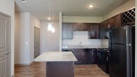 This thoughtfully designed 2-bedroom, 3-bathroom residence in Magnolia offers a functional and modern single-floor layout. The open-concept kitchen is a standout feature, showcasing rich dark cabinetry, granite countertops, black appliances, and a central island with pendant lighting overhead — seamlessly connecting to the living area, which is finished with hardwood-style flooring and carpeted transitions. Natural light flows generously through large windows fitted with blinds, complemented by ceiling fans in both the living area and bedrooms. Each bedroom features plush carpeting, a ceiling fan, and its own window with outdoor views. The primary bedroom connects directly to a private en-suite bathroom, which includes a granite-topped dark vanity, dual mirrors, and direct access to a spacious walk-in closet with built-in shelving. Additional bathrooms echo the same refined finishes, maintaining design consistency throughout. A dedicated laundry room provides in-unit washer and dryer hookups for added convenience. With six closets, two hallways, and a utility room, storage and practicality are prioritized throughout. The neutral color palette and cohesive design elements lend the space a clean, modern ambiance.