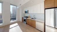 Located in the heart of Downtown Los Angeles at 427 W 5th Street, this modern single-floor unit offers a clean, contemporary design with an open and airy layout. Light hardwood flooring runs throughout the living areas and bedrooms, complementing the crisp white walls and contributing to a bright, welcoming atmosphere.

The kitchen is thoughtfully designed with two-tone cabinetry — warm wood lower cabinets paired with sleek white upper cabinets — along with a white tile backsplash, stainless steel appliances including a gas range, microwave, and dishwasher, and a white quartz countertop. A floor-to-ceiling window floods the kitchen and adjoining living area with natural light and frames sweeping views of the Downtown LA skyline.

The bedroom is generously sized, featuring large corner windows that frame panoramic city views and allow abundant sunlight to fill the space. A secondary room offers a more intimate setting with a horizontal window, providing additional natural light.

The bathroom is finished with large-format tile in the soaking tub and shower enclosure, warm wood open shelving, a sleek vanity with a white countertop, and a backlit mirror — combining modern functionality with refined aesthetics.

A well-proportioned entryway hallway with a closet leads into the open living space, completing this thoughtfully designed urban retreat.
