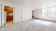 Located at 2220 W Layton Ave in Milwaukee, WI, this two-bedroom, one-bathroom unit offers a practical and straightforward layout across a single floor. The living area is carpeted in neutral gray tones and benefits from natural light that filters through the windows, with a baseboard heating system running along the walls to ensure comfort year-round. A wood-paneled entry door leads into the space, which connects to the rest of the unit via a central hallway. The generously sized primary bedroom features carpeted flooring, a closet with wood-tone doors, and a baseboard heater, while a window frames views of surrounding greenery. The second bedroom is similarly appointed with carpet, a closet, and its own baseboard heating unit, making it well-suited as a guest room or home office. The kitchen features warm wood-toned cabinetry providing ample storage. The bathroom is finished with classic tilework, including a mosaic tile floor and tiled tub surround, complemented by a wall-mounted sink and mirror. Throughout the unit, the clean white walls and neutral finishes create a simple, functional ambiance that offers a blank canvas for personalization.