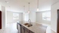 This well-appointed 2-bedroom, 3-bathroom single-floor residence offers a thoughtfully designed open-concept layout with contemporary finishes throughout. The combined kitchen and living area serves as the heart of the home, featuring light hardwood-style flooring, multiple windows that invite natural light, and vertical blinds for privacy. The kitchen is a standout, centered around a large granite-topped island with a double stainless steel sink and pendant lighting overhead. Dark cabinetry, stainless steel appliances — including a refrigerator, range, and microwave — complete the functional and stylish space. The living area flows naturally from the kitchen, creating a bright and open atmosphere. Both bedrooms are carpeted for comfort, with the primary bedroom offering a generous footprint and windows with outdoor views. The bathrooms are finished with dark wood vanities, white countertops, and tile flooring. Accessibility features, including grab bars in the tub/shower areas, are thoughtfully incorporated. A tucked-away in-unit laundry closet houses a full-size washer and dryer with overhead shelving. Two closets provide additional storage, rounding out this efficient and modern living space.
