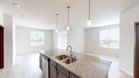 This well-appointed 2-bedroom, 3-bathroom single-floor residence offers a thoughtfully designed open-concept layout with contemporary finishes throughout. The combined kitchen and living area serves as the heart of the home, featuring light hardwood-style flooring, multiple windows that invite natural light, and vertical blinds for privacy. The kitchen is a standout, centered around a large granite-topped island with a double stainless steel sink and pendant lighting overhead. Dark cabinetry, stainless steel appliances — including a refrigerator, range, and microwave — complete the functional and stylish space. The living area flows naturally from the kitchen, creating a bright and open atmosphere. Both bedrooms are carpeted for comfort, with the primary bedroom offering a generous footprint and windows with outdoor views. The bathrooms are finished with dark wood vanities, white countertops, and tile flooring. Accessibility features, including grab bars in the tub/shower areas, are thoughtfully incorporated. A tucked-away in-unit laundry closet houses a full-size washer and dryer with overhead shelving. Two closets provide additional storage, rounding out this efficient and modern living space.
