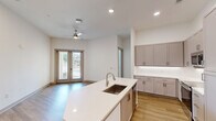 Located at 16035 Likely Ln in Huntersville, NC, this well-appointed one-bedroom, one-bathroom residence offers a thoughtfully designed single-floor layout with a generous overall footprint. The open-concept kitchen and living area serves as the heart of the home, featuring a large central island with a white quartz countertop and integrated sink, complemented by gray shaker-style cabinetry extending to the ceiling for ample storage. Stainless steel appliances, including a range, microwave, and French door refrigerator, complete the kitchen. Light wood-style flooring flows seamlessly throughout the entire unit, adding warmth and continuity. The spacious living area is bright and airy, with recessed lighting and a sliding glass door that invites natural light and provides outdoor views. The bedroom offers multiple windows fitted with blinds, allowing for versatile light control, and connects to a well-organized walk-in closet with built-in shelving and hanging rods for efficient storage. The bathroom is clean and modern, featuring a full tub and shower combination with white subway tile surround, brushed nickel fixtures, and a white vanity with quartz countertop. The entrance provides a welcoming transition into the open living spaces beyond.