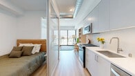 Located at 10401 Washington Blvd in Culver City, this thoughtfully designed studio unit offers a compact yet highly functional single-floor layout. The open-concept living and kitchen area serves as the heart of the space, featuring light oak hardwood flooring that runs throughout and an exposed metallic duct system that adds an industrial-modern character to the ceiling.

The kitchen is outfitted with full-height cabinetry in a soft grey-white palette, white quartz countertops, a textured tile backsplash, and a complete suite of stainless steel appliances including a gas range, built-in microwave, dishwasher, and refrigerator. The living area is bright and airy, anchored by a large floor-to-ceiling sliding glass door that opens to a balcony and frames sweeping city views, flooding the space with natural light.

The sleeping area is cleverly separated from the main living zone by a floor-to-ceiling glass sliding partition, providing privacy while maintaining an open feel. A hallway with recessed lighting connects the rooms and houses a wall-mounted thermostat for climate control.

The bathroom is clean and modern, featuring a single vanity with white countertop, soft grey cabinetry, brushed nickel fixtures, a large mirror with an elegant wall-mounted light fixture, and a separate shower enclosure with light tile finishes.