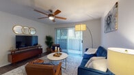 This single-floor residence offers a thoughtfully designed layout that balances comfort and functionality throughout its key living spaces. The living room serves as the heart of the home, featuring wood-style flooring, a ceiling fan with light fixture, and a sliding glass door dressed with vertical blinds that invites natural light and provides access to the outdoors. The space accommodates a relaxed, mid-century modern aesthetic with ample room for seating and entertaining. Adjacent to the living area, a dedicated dining nook provides an intimate setting for meals, accented by a window with slatted blinds that brings in additional natural light. The kitchen is equipped with stainless steel appliances — including a full-size refrigerator, electric range, and microwave — complemented by rich wood cabinetry, granite-style countertops, a skylight feature, and durable wood-look flooring. The bedroom is a serene retreat, offering generous proportions, a ceiling fan, hardwood-style flooring, and windows that allow soft natural light to filter in. The bathroom features a granite-topped vanity with warm wood cabinetry, a large mirror, wood-look tile flooring, and a shower-tub combination. Throughout the residence, neutral tones and consistent flooring create a cohesive and inviting atmosphere.