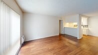 Located at 2020 W Alameda Ave in Anaheim, CA, this one-bedroom, one-bathroom unit offers a well-organized and functional single-floor layout. The living room serves as the heart of the space, featuring warm hardwood flooring, neutral white walls, a textured ceiling, and a large picture window fitted with vertical blinds that invites generous natural light and outdoor views of surrounding greenery. A wall-mounted A/C unit provides climate control. The living area flows directly into the galley-style kitchen, which is accessible via a pass-through counter. The kitchen is outfitted with white cabinetry, a double-basin sink, a white electric range, tile backsplash accenting, and a skylight overhead that brightens the workspace. The bedroom is a generously sized, carpeted retreat featuring a sliding-door closet with built-in shelving and rod, a window with an outdoor view, and a textured ceiling. An additional open closet with shelving is found in a secondary area off the main hall. The bathroom is clean and bright, featuring a white vanity with a large mirror, a tub/shower combo, and hardwood-style flooring. Throughout the unit, the light color palette and consistent finishes create a cohesive, practical living environment.