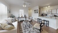 Located at 9821 Chapel Rd in Waco, Texas, this single-story home offers a thoughtfully designed open-concept layout with warm, neutral tones throughout. The living area is bright and welcoming, featuring hardwood-style flooring, crown molding, a ceiling fan with light fixture, and large windows fitted with blinds that allow generous natural light to fill the room. The kitchen is well-appointed with white cabinetry accented by wood trim, ample counter space, a peninsula with bar seating, a range, microwave, and refrigerator — all finished in white. Track lighting overhead adds a practical touch. Adjacent to the kitchen, a dedicated dining area offers a formal setting with a full-size dining table, large window, and a pass-through mirror that visually connects the space to the living area. The bedrooms are carpeted and finished with crown molding, each featuring ceiling fans or overhead lighting. One bedroom includes a bay window configuration, flooding the room with natural light, while another features mirrored closet doors and a walk-in closet with built-in shelving. The bathroom includes a full tub and shower combination with white tile surround. Throughout the home, the consistent use of light, neutral finishes creates a cohesive and comfortable ambiance.