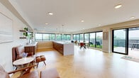 Located at 5545 Park Ave in Fairfield, CT, this single-floor community space offers a generously sized, thoughtfully designed interior that seamlessly connects with a substantial outdoor terrace. The interior features striking herringbone-patterned light hardwood flooring throughout, recessed lighting, and a neutral warm color palette that creates a bright, welcoming atmosphere.

The open-plan layout integrates a full kitchen anchored by a large white-topped island with walnut cabinetry and pendant lighting, alongside a dining area and multiple lounge zones. Floor-to-ceiling black-framed windows and sliding glass doors line the perimeter, flooding the space with natural light and offering unobstructed views of the outdoor terrace and surrounding greenery.

A separate lounge area provides a more intimate setting, furnished with leather accent chairs, round decorative mirrors, and soft seating arrangements, connected to the main open space via a glass-paneled door.

The expansive outdoor terrace is a standout feature, comprising large-format tiled decking, a pergola strung with bistro lighting, artificial turf sections with lounge chairs, and outdoor dining furniture — ideal for gatherings and events. The combination of modern architecture, abundant natural light, and indoor-outdoor connectivity makes this a highly functional and visually impressive multi-purpose space.