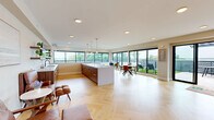 Located at 5545 Park Ave in Fairfield, CT, this single-floor community space offers a generously sized, thoughtfully designed interior that seamlessly connects with a substantial outdoor terrace. The interior features striking herringbone-patterned light hardwood flooring throughout, recessed lighting, and a neutral warm color palette that creates a bright, welcoming atmosphere.

The open-plan layout integrates a full kitchen anchored by a large white-topped island with walnut cabinetry and pendant lighting, alongside a dining area and multiple lounge zones. Floor-to-ceiling black-framed windows and sliding glass doors line the perimeter, flooding the space with natural light and offering unobstructed views of the outdoor terrace and surrounding greenery.

A separate lounge area provides a more intimate setting, furnished with leather accent chairs, round decorative mirrors, and soft seating arrangements, connected to the main open space via a glass-paneled door.

The expansive outdoor terrace is a standout feature, comprising large-format tiled decking, a pergola strung with bistro lighting, artificial turf sections with lounge chairs, and outdoor dining furniture — ideal for gatherings and events. The combination of modern architecture, abundant natural light, and indoor-outdoor connectivity makes this a highly functional and visually impressive multi-purpose space.