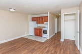 Located at 2120 Bryanston Ct in Detroit, MI, this single-floor unit offers a straightforward, functional layout designed for comfortable everyday living. The open living and kitchen area forms the heart of the space, where warm hardwood-style flooring extends throughout, contrasting with light tile in the kitchen zone. The kitchen is equipped with rich cherry-toned cabinetry providing ample upper and lower storage, a laminate countertop with a stainless steel sink, a white electric range with overhead ventilation, and a full-size refrigerator. A textured ceiling runs throughout the unit, contributing to its classic character. The living area is generously proportioned, offering flexible arrangements for furniture, and benefits from natural light streaming through a wide sliding window fitted with vertical blinds. A baseboard heating unit runs beneath the window, ensuring warmth during Detroit's colder months. A hallway connects the living space to the bedroom and bathroom, with a closet featuring built-in shelving providing convenient storage. The bathroom is clean and bright, finished with light tile flooring, a rich wood vanity with a white countertop, a large mirror, and a full tub-shower combination.