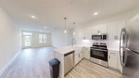 Located at 5 View Lake Dr in Clayton, NC, this well-appointed single-story home offers 2 bedrooms and 2 bathrooms within a thoughtfully designed floor plan. The open-concept kitchen and living area serves as the heart of the home, showcasing white shaker-style cabinetry, a classic subway tile backsplash, and a large quartz-topped peninsula illuminated by sleek pendant lights. Stainless steel appliances, including a range, microwave, dishwasher, and refrigerator, complete the kitchen. Light wood-look flooring flows throughout the main living areas, creating a bright and cohesive aesthetic. The living room receives generous natural light through multiple windows with views to the outdoors. Both bedrooms feature plush carpeting and ample closet space, with the primary bedroom offering a generously sized layout and an en-suite bathroom equipped with a quartz vanity and a glass-enclosed shower. The second bathroom includes a full tub-shower combination and a matching white vanity. The home also includes a dedicated laundry area, a utility room, and an impressive six closets, providing abundant storage. The clean, neutral palette and modern finishes throughout give this home a fresh, move-in-ready appeal.