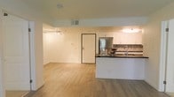 This single-floor space offers a clean, contemporary layout with an open-concept design that connects the living area and kitchen in one cohesive space. Light wood-look flooring extends throughout, lending warmth and visual continuity to the interior.

The kitchen is well-appointed with crisp white cabinetry, dark countertops, and stainless steel appliances, including a full-size refrigerator. A decorative mosaic tile backsplash adds a touch of texture and color, complementing the kitchen's modern aesthetic. A breakfast bar peninsula provides additional counter space and creates a natural transition into the main living area.

The living area is open and versatile, with neutral white walls and track lighting that allow for flexible furniture arrangements and personalization. A standard entry door with a secure deadbolt is positioned centrally, providing convenient access. Overhead HVAC vents are integrated cleanly into the ceiling, ensuring efficient climate control throughout the space.

Overall, the space presents a bright, functional, and modern environment, ideal for those who appreciate a streamlined, open layout with practical design details.