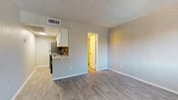 This single-floor unit offers a clean, functional layout with modern finishes throughout. The main living area is open and airy, featuring light gray laminate flooring, neutral-toned walls, and a textured ceiling. A window in the bedroom area allows natural light to fill the space, offering views of surrounding greenery. The kitchen is positioned adjacent to the living area in a galley-style configuration, equipped with white cabinetry featuring sleek bar-pull hardware, marble-look countertops, a stainless steel sink, a tile backsplash in warm neutral tones, and stainless steel appliances including a refrigerator and electric range. A pass-through counter connects the kitchen to the living space, enhancing the open feel. The bathroom is well-appointed with a white vanity cabinet topped with a marble-look surface, a framed mirror, a single-basin sink with a brushed nickel faucet, and hardwood-style flooring that continues from the rest of the unit. The bedroom is accessed through a doorway from the main living area and benefits from a window with blinds, providing both privacy and natural light. Throughout the unit, consistent flooring, white baseboards, and a neutral color palette create a cohesive and move-in ready environment.