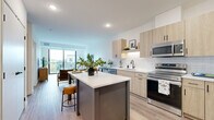 Located at 11816 Wayzata Blvd in Minnetonka, MN, this thoughtfully designed one-bedroom, one-bathroom residence offers a well-appointed single-floor layout with modern finishes and efficient use of space. The open-concept kitchen and living area serves as the heart of the home, where light wood cabinetry, white subway tile backsplash, and stainless steel appliances — including a full-size refrigerator, range, and microwave — create a sleek, contemporary kitchen. A central island with seating provides additional prep space and a casual dining option. The living area is bright and airy, benefiting from large floor-to-ceiling sliding glass doors that open onto a private balcony with outdoor views, flooding the space with natural light. Durable light-toned luxury vinyl plank flooring runs throughout the main areas, adding warmth and cohesion. The bedroom is a comfortable retreat featuring plush carpeting, a ceiling fan, and windows that frame pleasant outdoor views. The full bathroom is finished with a light wood vanity, white quartz countertop, a soaking tub and shower combination, and coordinating black hardware accents. Practical conveniences include in-unit stacked laundry and three closets for generous storage throughout.