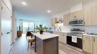 Located at 11816 Wayzata Blvd in Minnetonka, MN, this thoughtfully designed one-bedroom, one-bathroom residence offers a well-appointed single-floor layout with modern finishes and efficient use of space. The open-concept kitchen and living area serves as the heart of the home, where light wood cabinetry, white subway tile backsplash, and stainless steel appliances — including a full-size refrigerator, range, and microwave — create a sleek, contemporary kitchen. A central island with seating provides additional prep space and a casual dining option. The living area is bright and airy, benefiting from large floor-to-ceiling sliding glass doors that open onto a private balcony with outdoor views, flooding the space with natural light. Durable light-toned luxury vinyl plank flooring runs throughout the main areas, adding warmth and cohesion. The bedroom is a comfortable retreat featuring plush carpeting, a ceiling fan, and windows that frame pleasant outdoor views. The full bathroom is finished with a light wood vanity, white quartz countertop, a soaking tub and shower combination, and coordinating black hardware accents. Practical conveniences include in-unit stacked laundry and three closets for generous storage throughout.