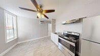 This single-floor studio is thoughtfully laid out to maximize every square foot of its compact footprint. The main living area is finished with light wood-look tile flooring that runs throughout, creating a cohesive and clean aesthetic. Neutral gray walls and white baseboards contribute to a bright, airy atmosphere, while multiple windows fitted with horizontal blinds invite natural light and offer views of the surrounding exterior. A ceiling fan with a built-in light fixture provides both comfort and additional illumination overhead.

The kitchen is integrated into the main living space and features white cabinetry, a stainless steel sink, a stainless steel electric range with a range hood above, and a stainless steel refrigerator. A wall-mounted air conditioning unit ensures year-round climate control. The kitchen area also provides direct access to the entry door, which is equipped with a secure deadbolt.

The bathroom is a compact, functional space with wood-look tile flooring that mirrors the rest of the unit. It includes a walk-in shower stall lined with large-format gray wood-look wall tiles and a light mosaic tile floor, complemented by a recessed ceiling light overhead. A toilet and a sink with cabinetry complete the bathroom's practical layout. Overall, the studio presents a clean, modern, and functional living environment.